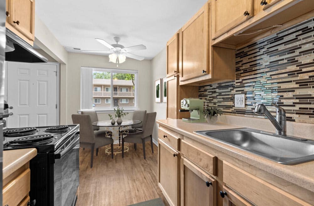 Modern kitchen with wooden cabinets, glass-top table, and tiled backsplash.