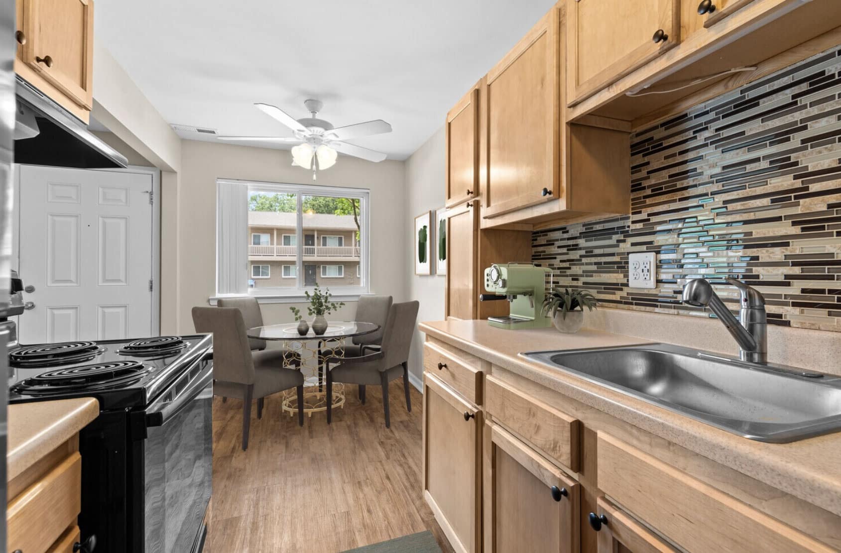 Modern kitchen with wooden cabinets, tiled backsplash, and dining area by a window.
